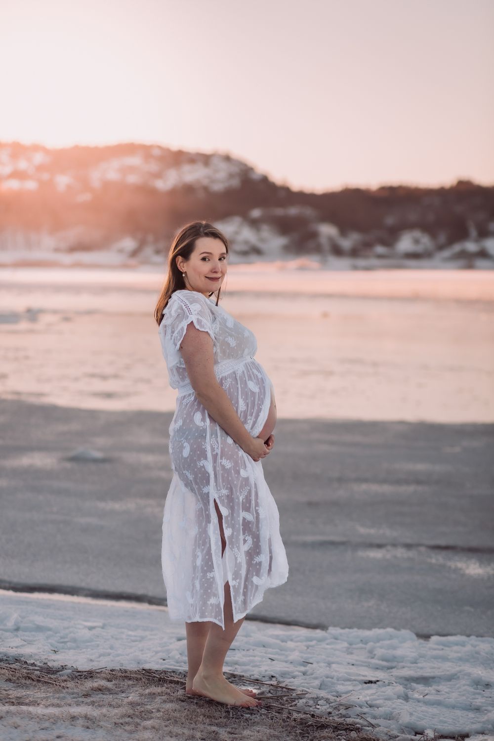 Person in white lace dress poses on beach during golden hour.