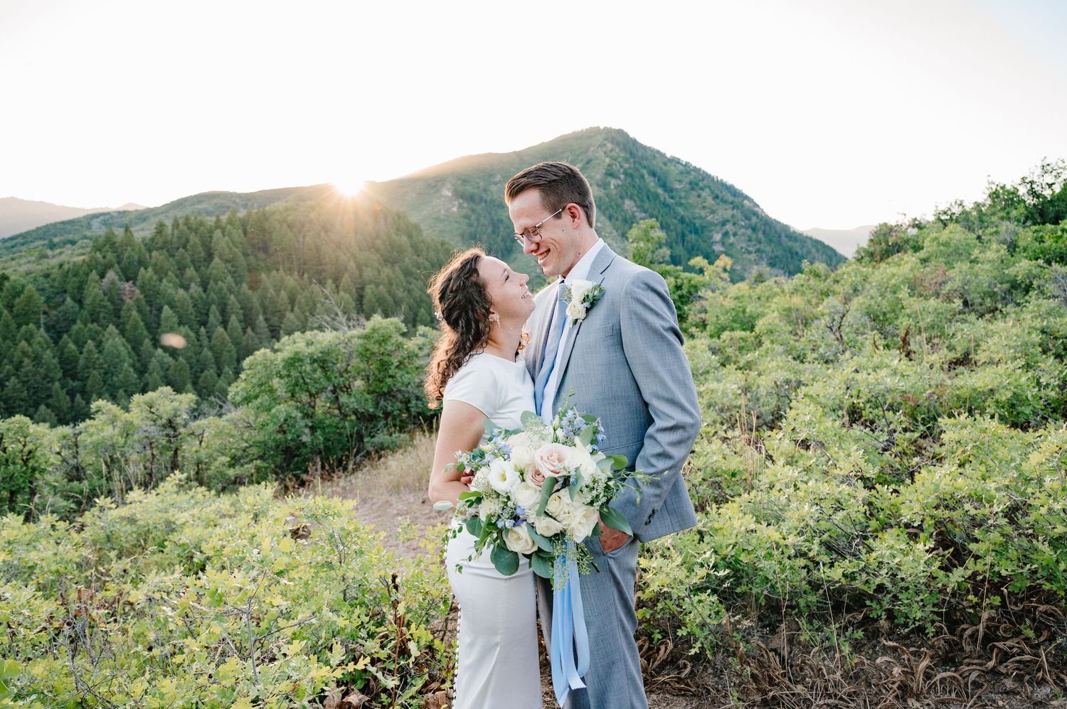 Romantic mountain wedding portrait with couple against scenic valley backdrop at sunset.