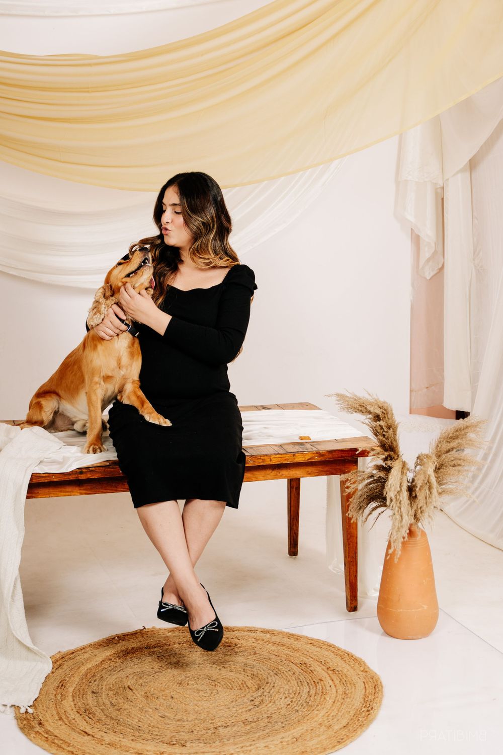 A lifestyle maternity photo with a golden retriever and woman in black dress sitting on wooden bench.