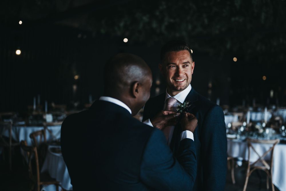 Groom having his button hold pinned on in the dutch barn at Grangefields