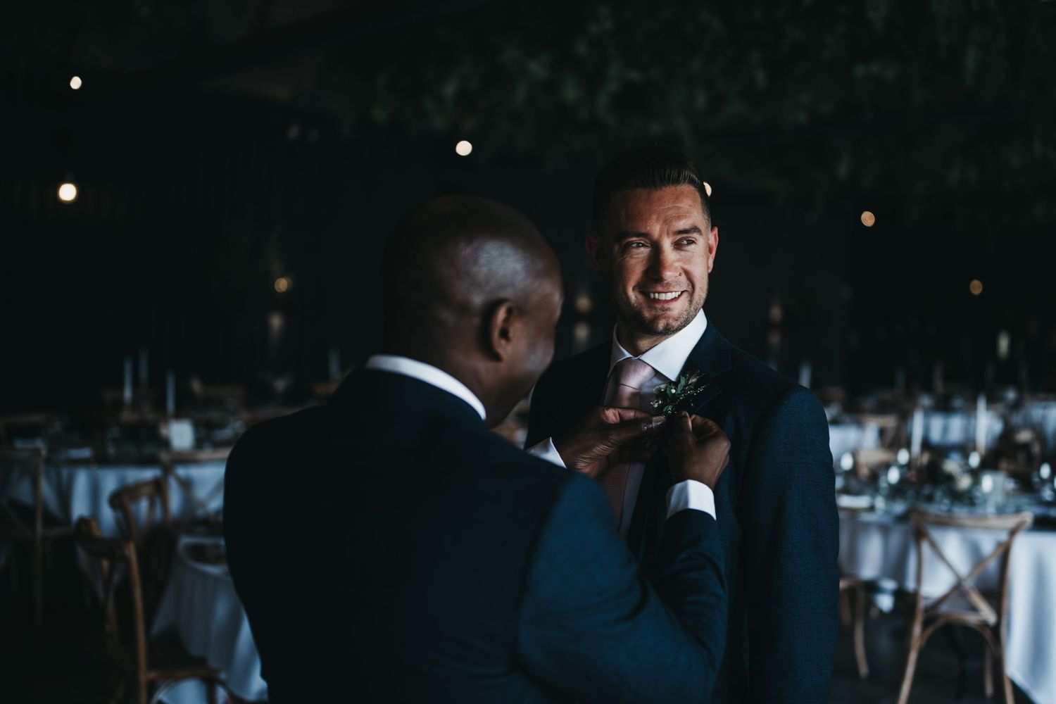 Groom having his button hold pinned on in the dutch barn at Grangefields