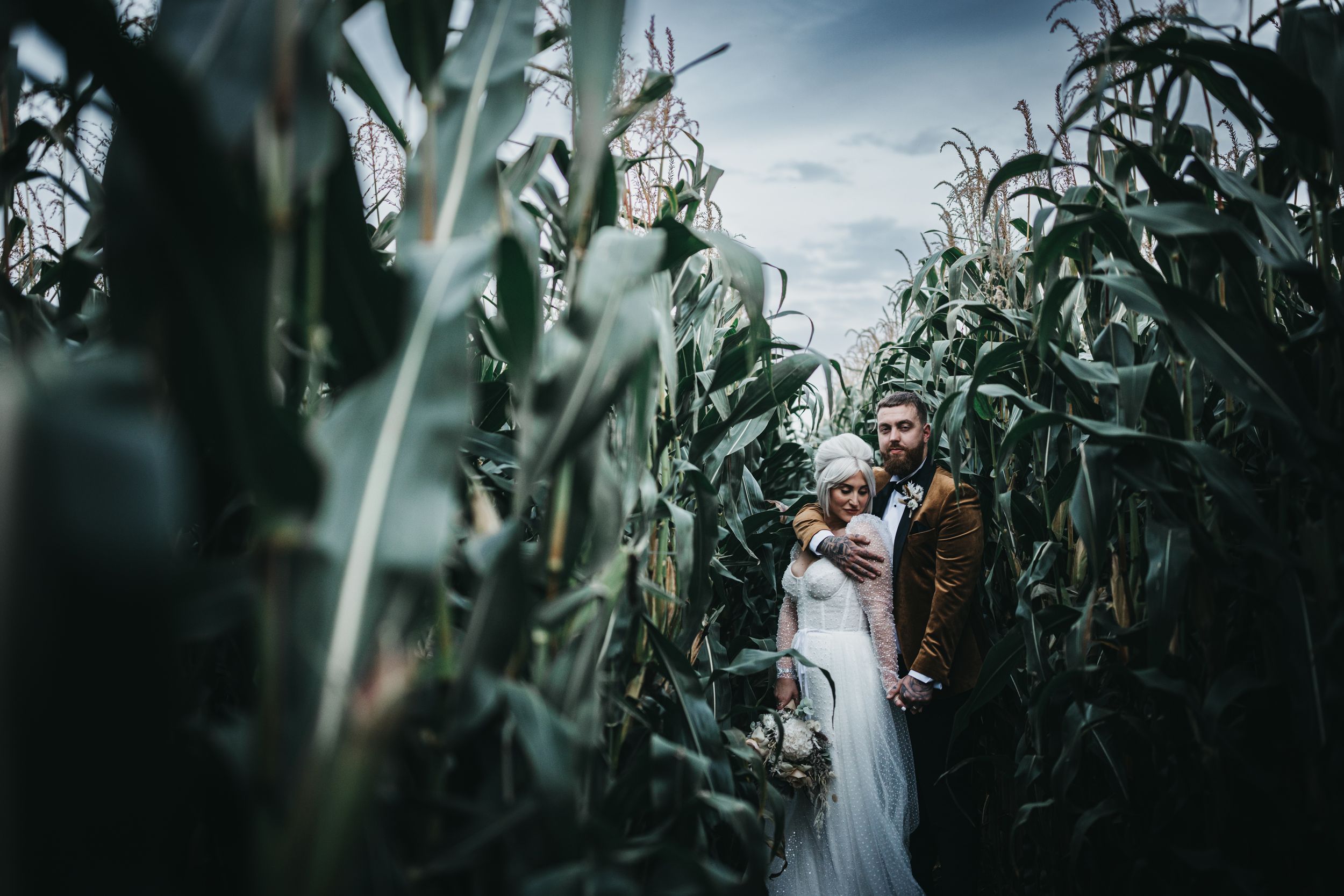 tattooed Bride and groom in cornfields holding each other