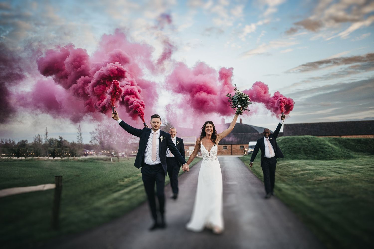 Pink Wedding smoke flares as couple walk up the road at Grangefields wedding venue