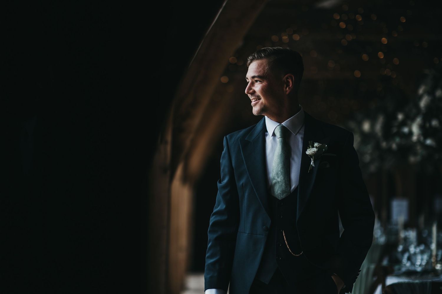 groom stood in window light of the oak barn in Swancar