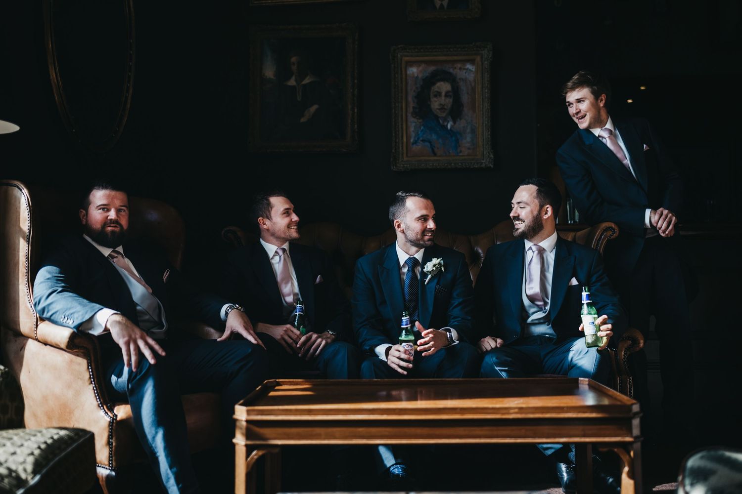 a groom and 4 groomsmen sit on a sofa in the brown bar at Stubton hall awaiting the wedding ceremony laughing