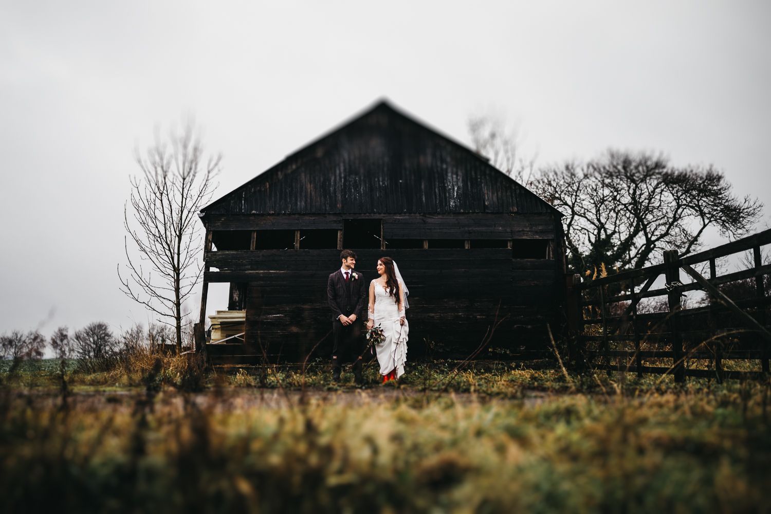 bride and groom in front of a black barn in countryside