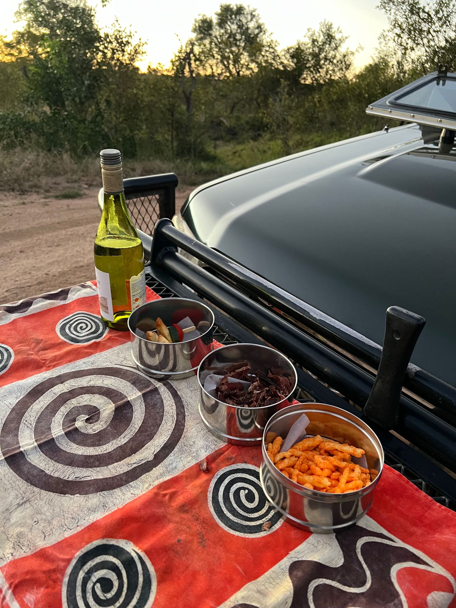 Outdoor dining setup with snacks and drinks on a colorful patterned tablecloth.