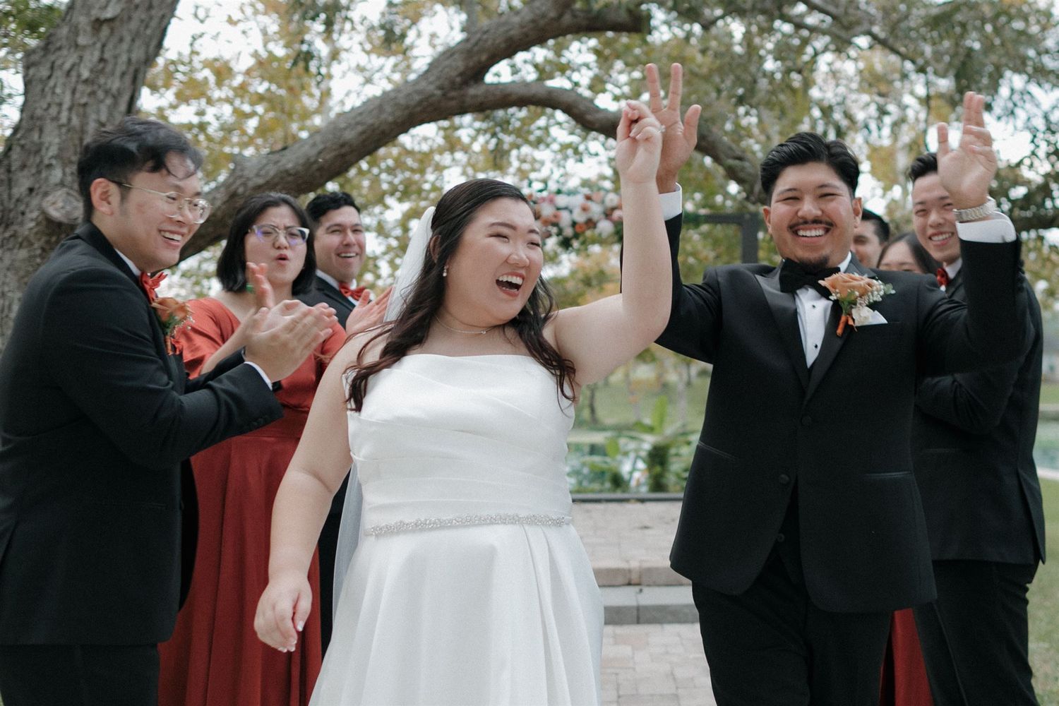 Wedding celebration with bridal party cheering and raising hands in excitement.