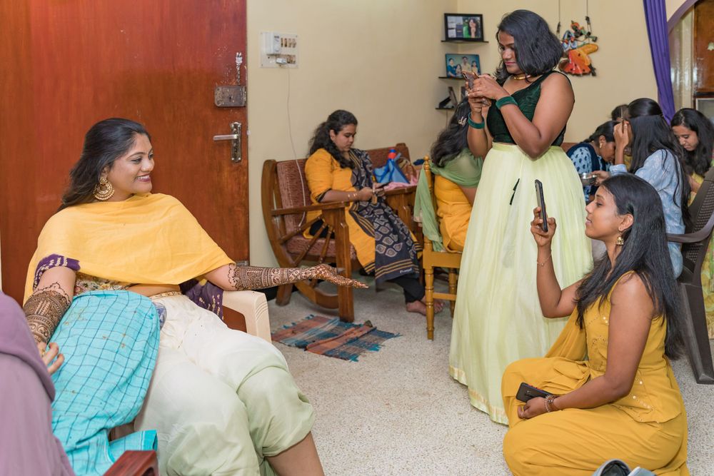 A lively indoor celebration with attendees wearing traditional Indian clothing in yellow and pastel shades.
