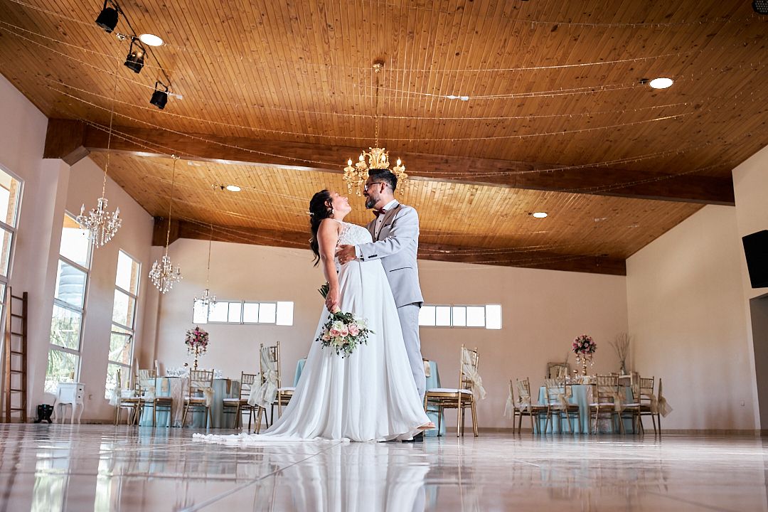 Elegant couple dancing alone in a spacious reception hall with wooden ceiling and aqua decor.