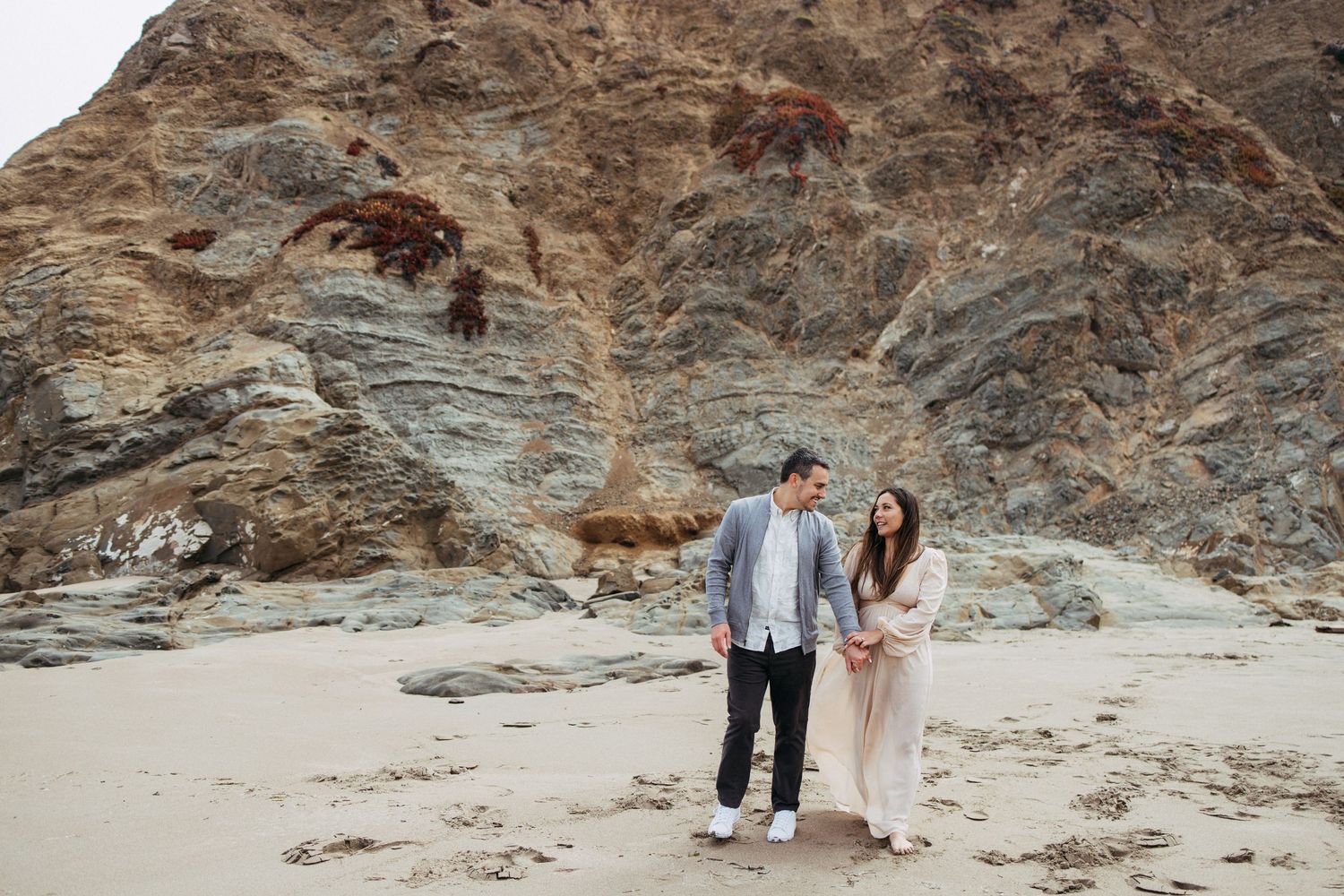 Couple in neutral clothes walk along Baker Beach for engagement portraits.