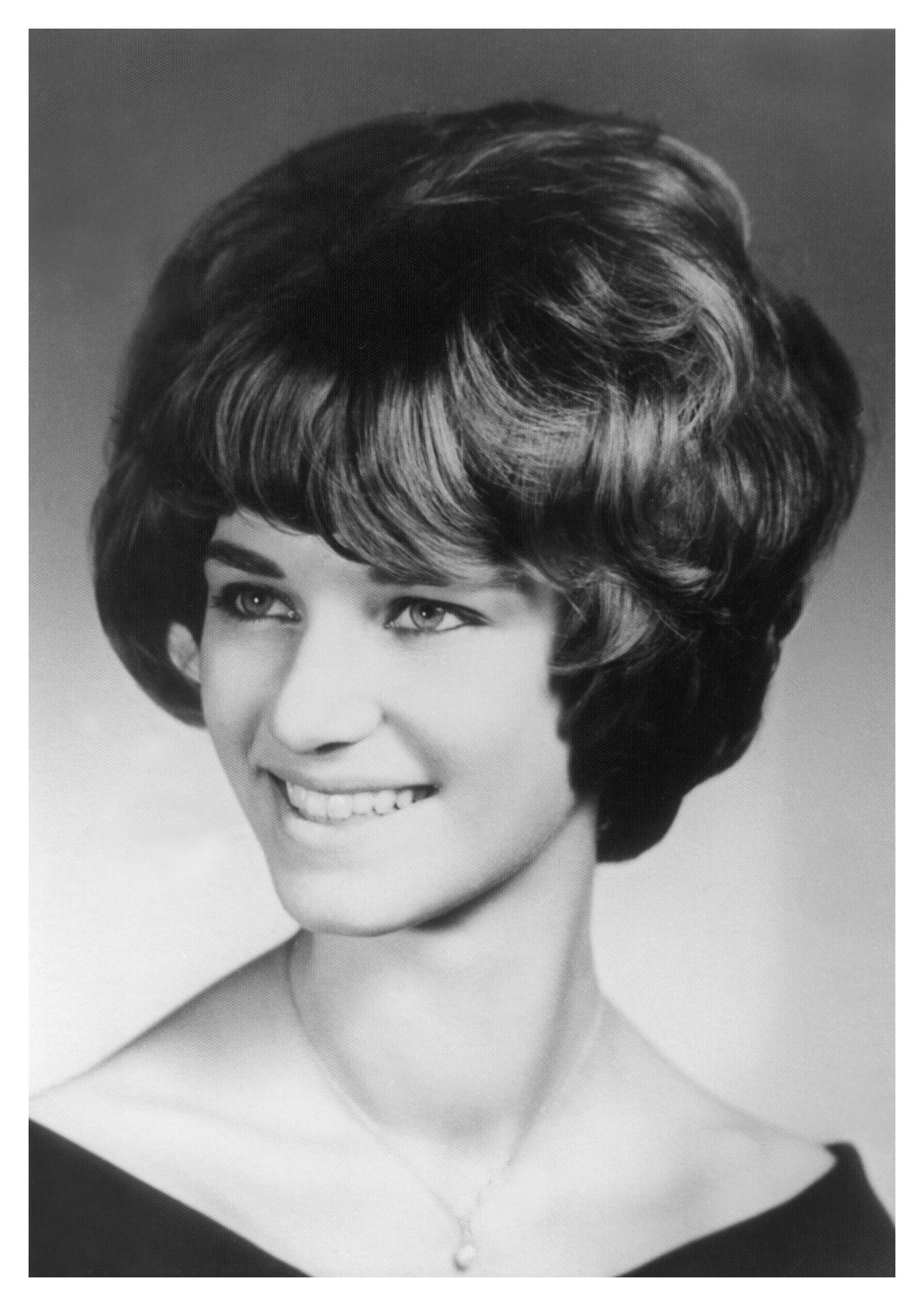 Black and white portrait of a woman with a 1960s bouffant hairstyle and warm smile.