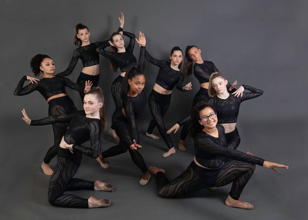 Dance group performing modern choreography in black outfits against grey background.