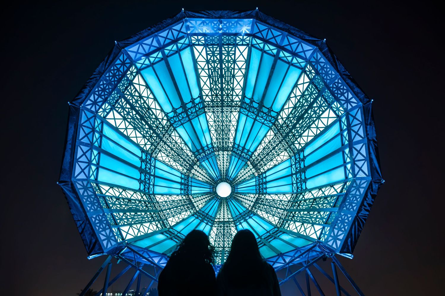 A glowing octagonal blue structure creates a radiant pattern against the dark night sky.