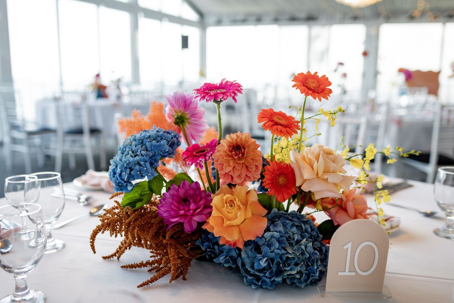 Vibrant floral centerpiece with blue hydrangeas, pink gerberas, and orange roses on an elegant table setting.
