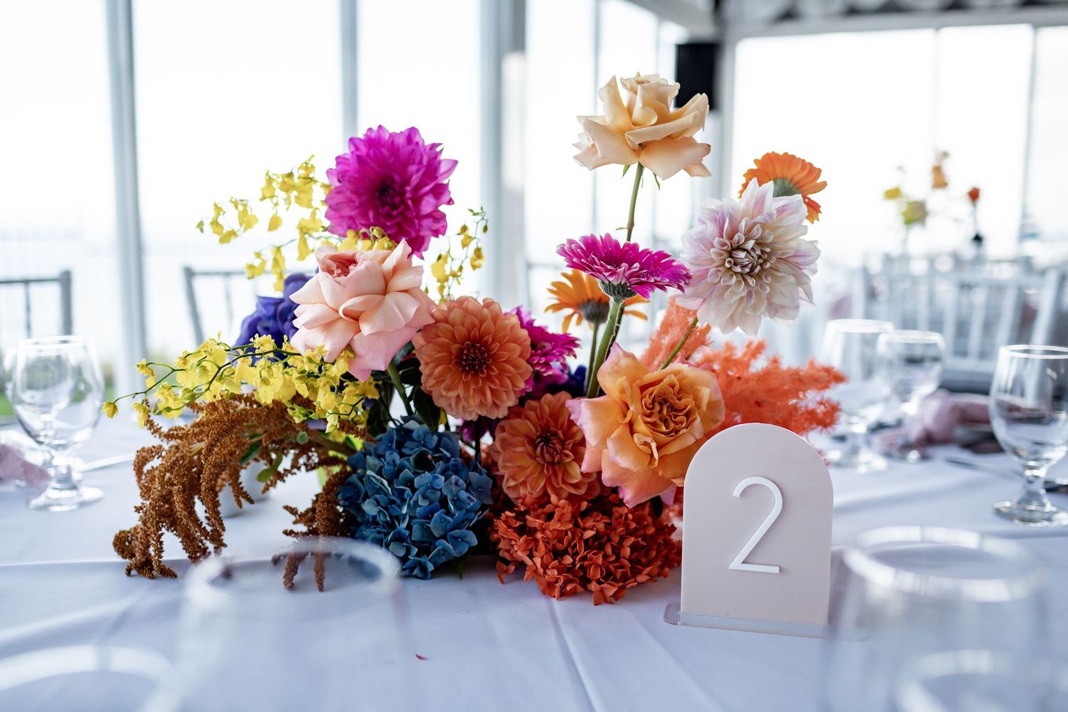 Colorful floral arrangement with pink dahlias and blue hydrangeas next to table number two.