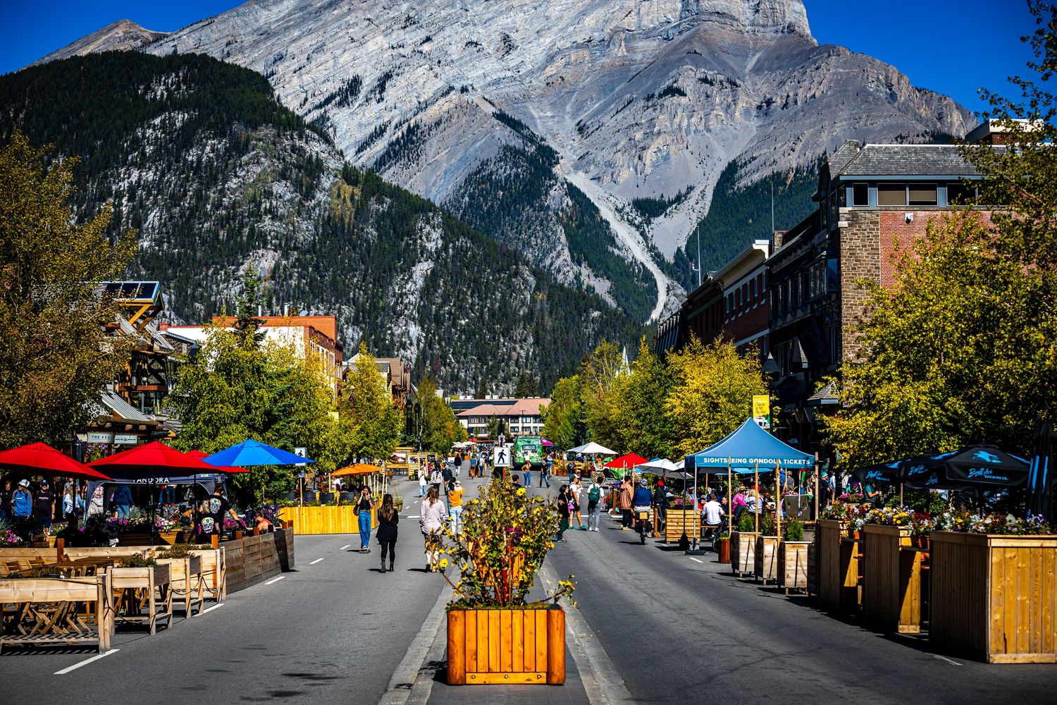 Bustling mountain town marketplace with shops and vendors beneath towering rocky peaks.