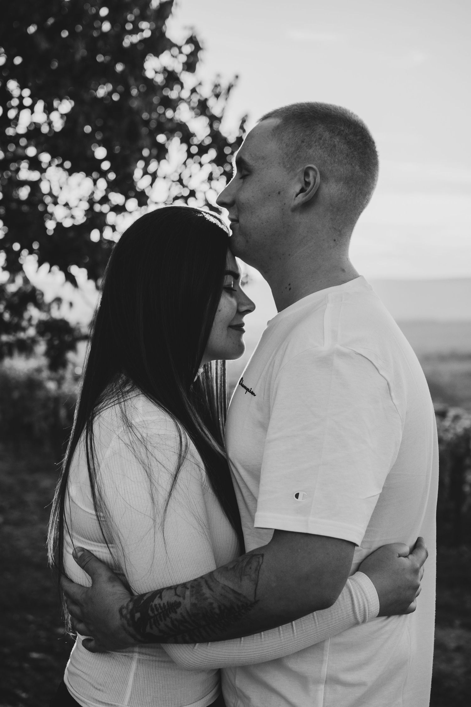 Black and white romantic portrait of couple embracing outdoors at sunset.