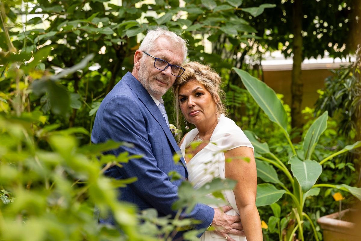 Couple shares an intimate moment in a garden setting surrounded by green foliage.