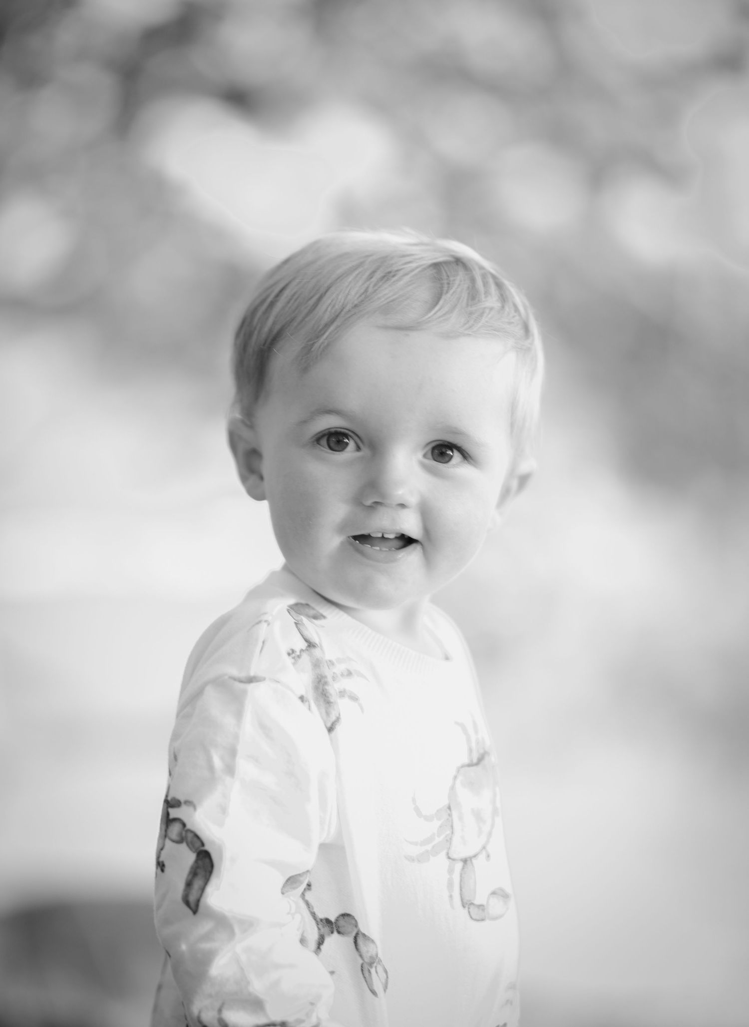 Young child in white dinosaur-print shirt poses for black and white portrait.
