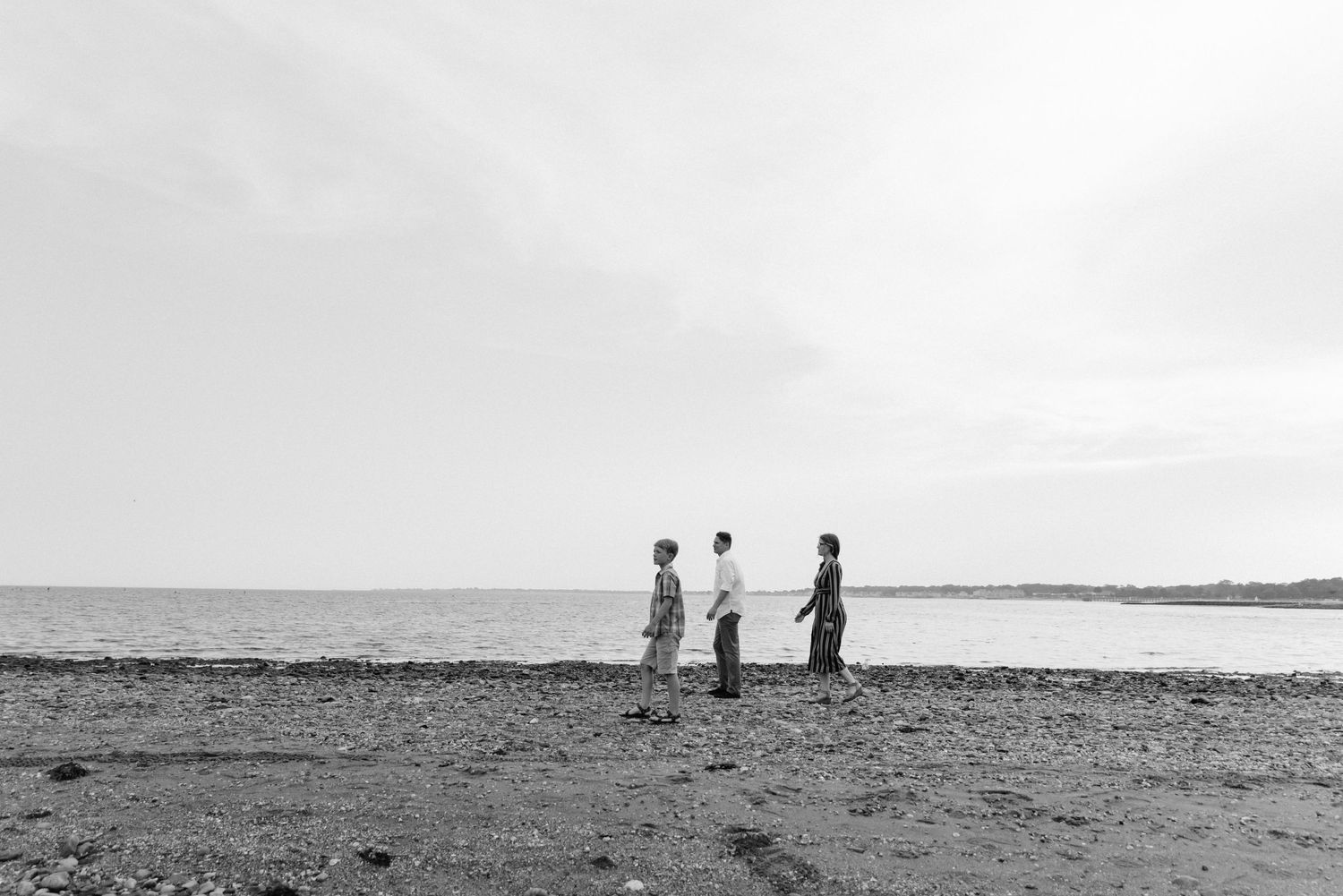 Three silhouettes stand on a beach against a minimalist black and white horizon.