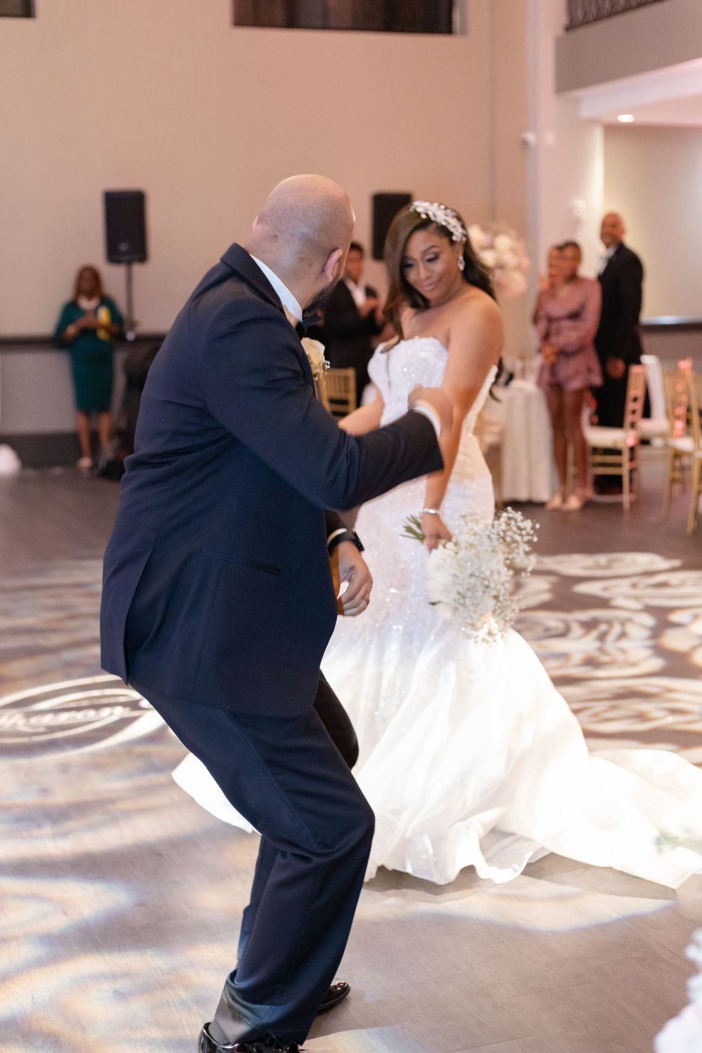 A couple shares a lively dance moment on a patterned ballroom floor at their wedding reception.