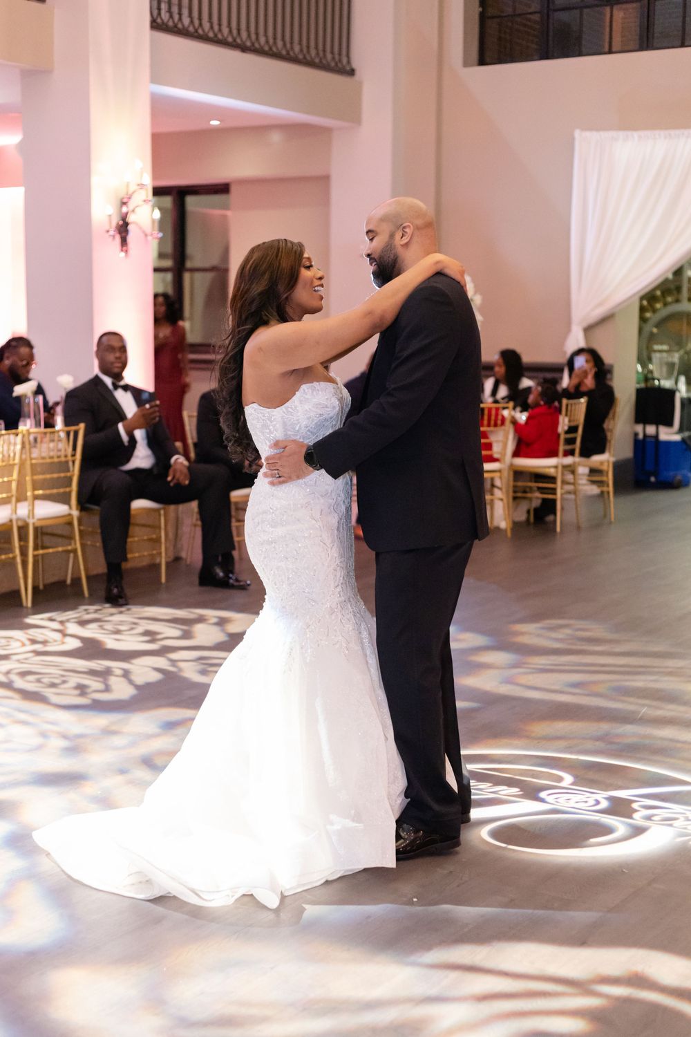 A couple shares an intimate slow dance moment at their wedding reception surrounded by guest tables.