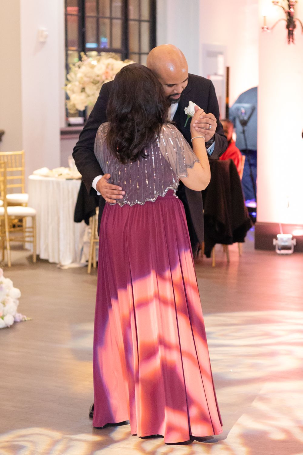 A couple dancing at a wedding reception with a woman wearing a sparkling burgundy dress.