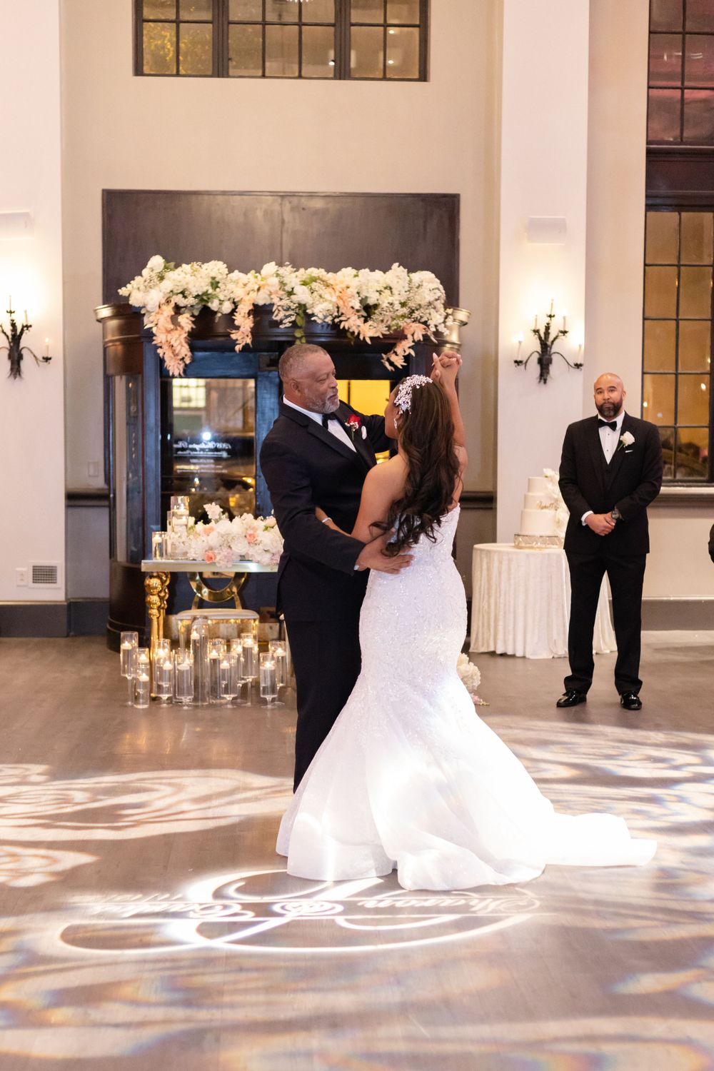 A wedding couple dances near an elegant fireplace display decorated with white orchids and candles.