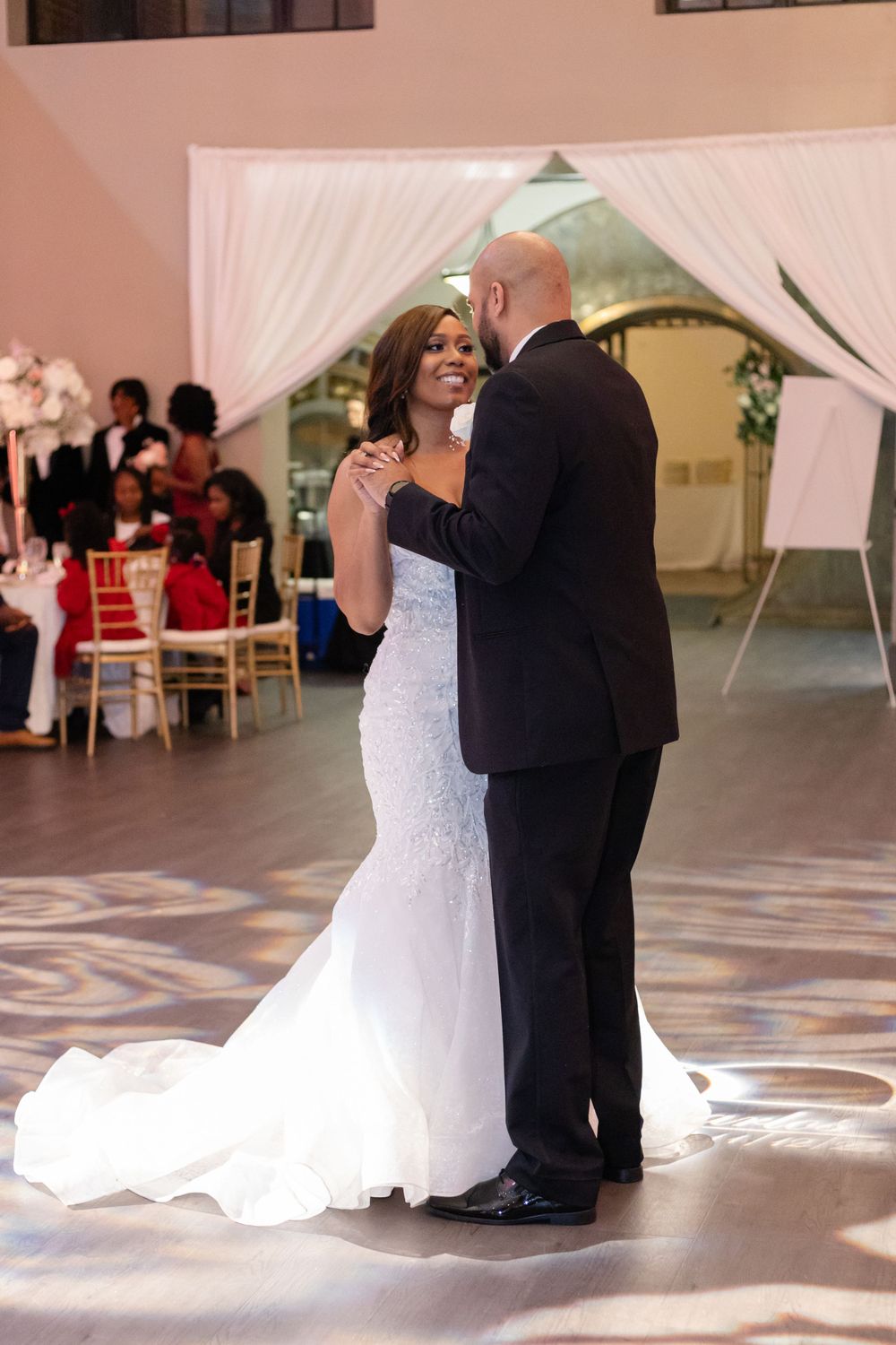 A couple shares their first dance in an elegantly decorated reception hall with pink lighting.