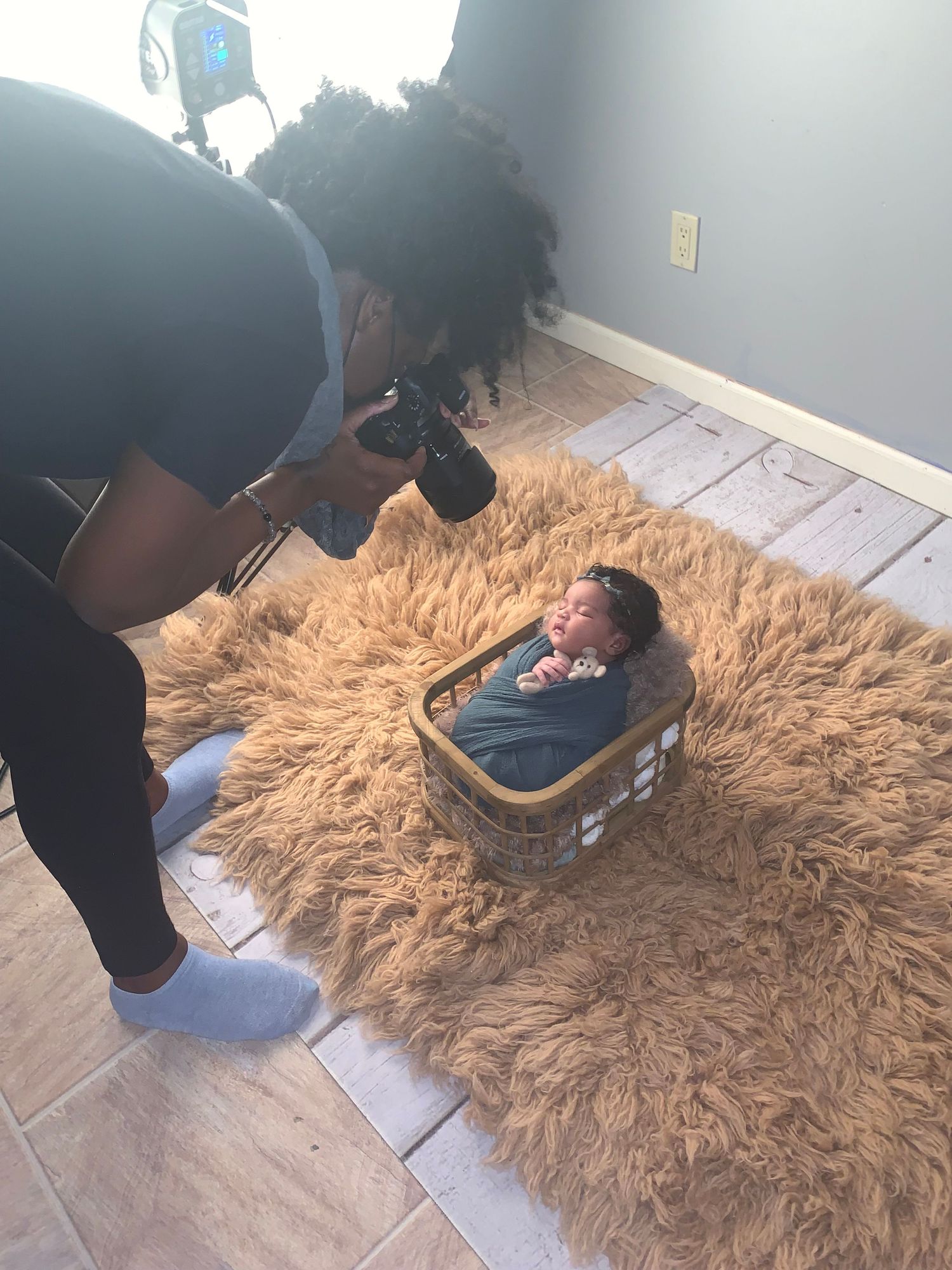 Photographer capturing newborn photo in vintage suitcase on furry brown rug.