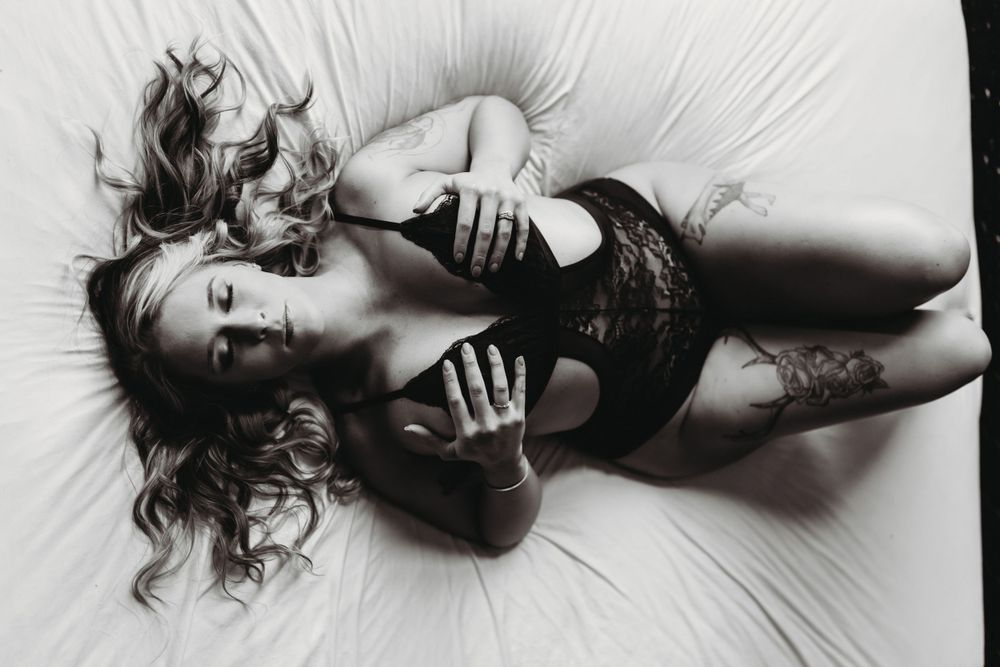 Black and white artistic boudoir photograph of a person in lace lingerie lying on a light background.