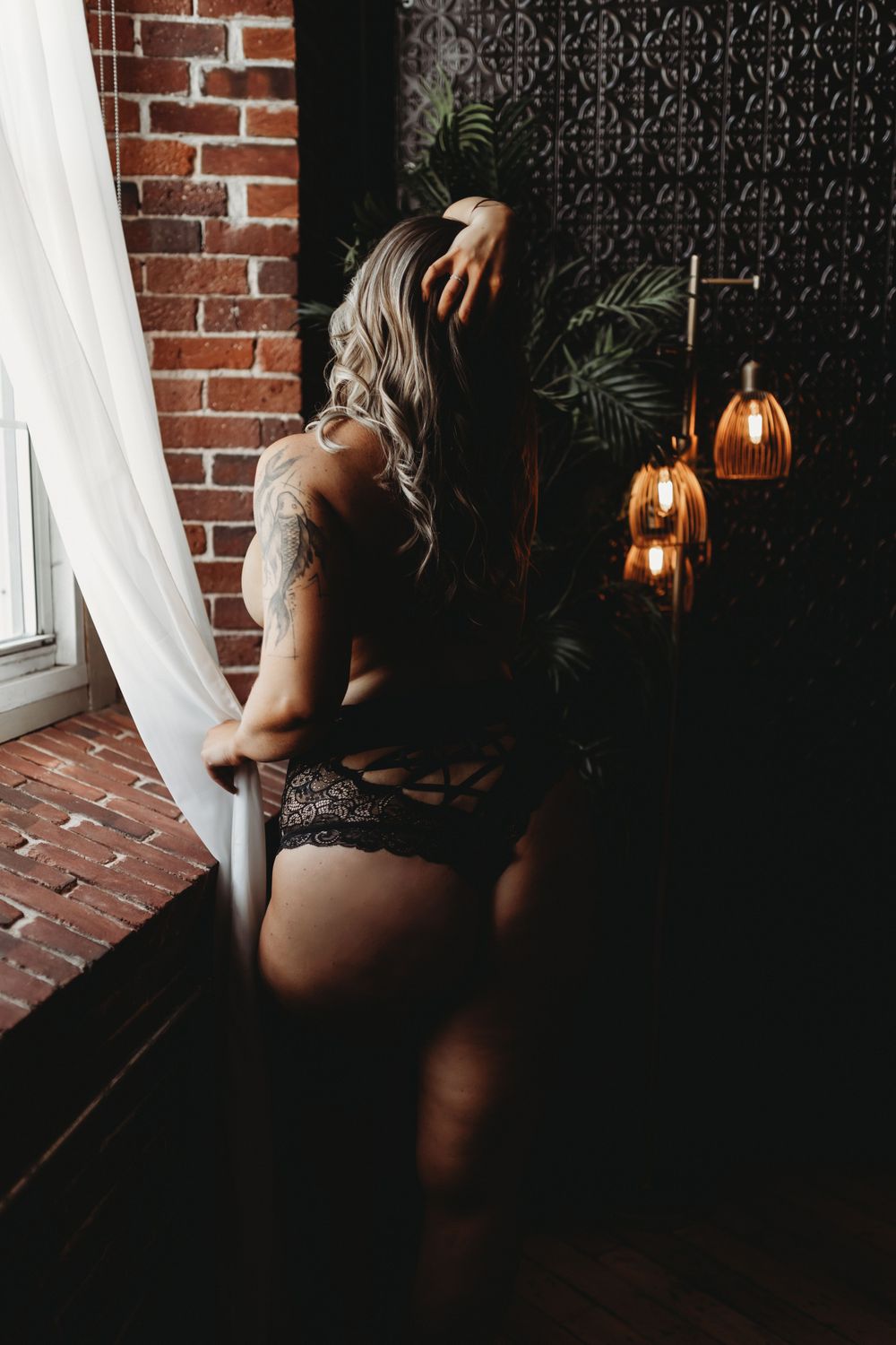 Sensual boudoir portrait with copper pendant lights and sheer curtains.