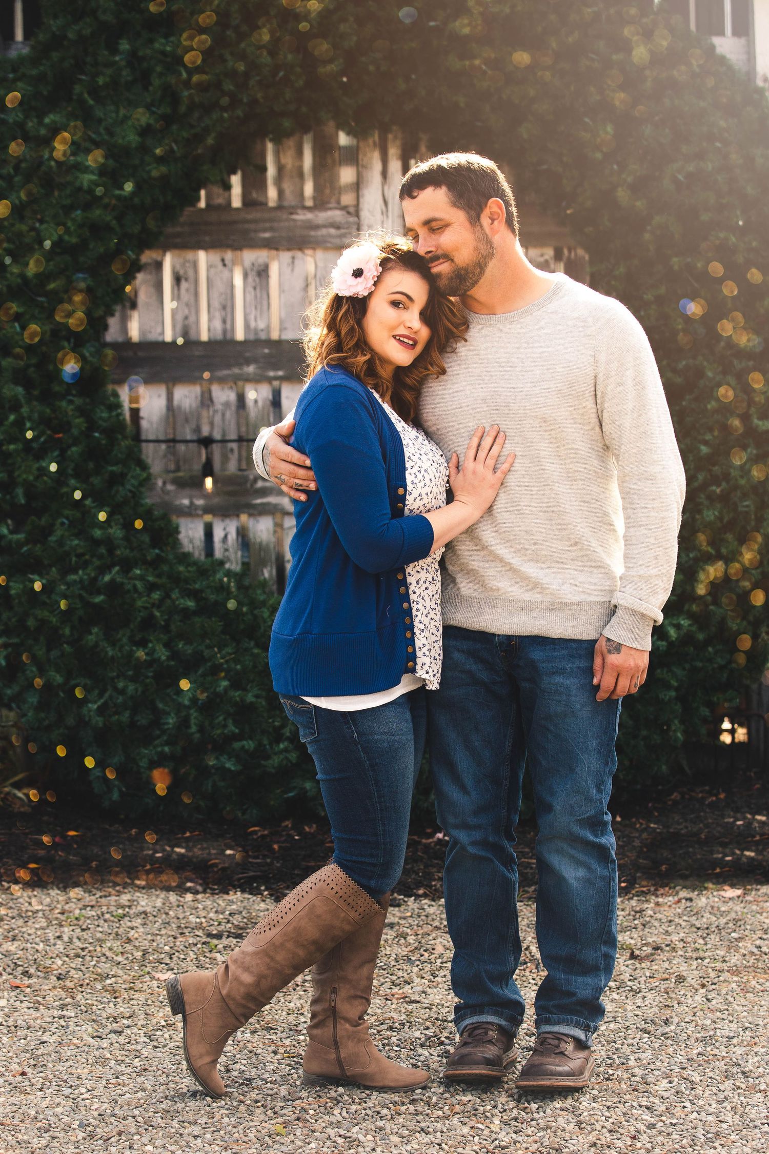 Couple embracing outdoors in warm golden sunlight near a rustic wooden fence in casual fall attire.