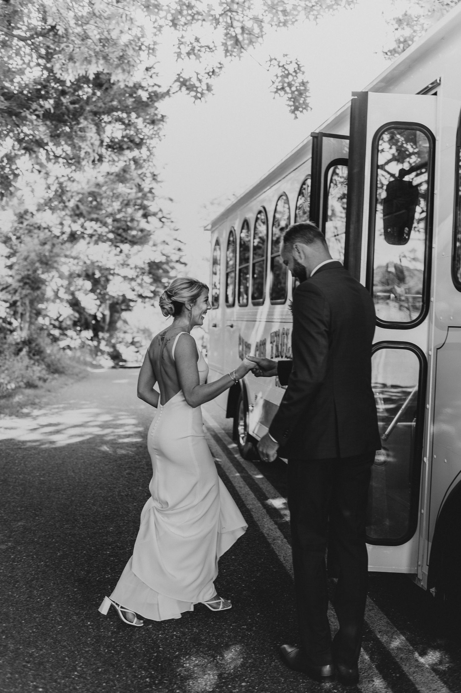 Black and white photo of newlyweds boarding a vintage-style trolley bus after their wedding.