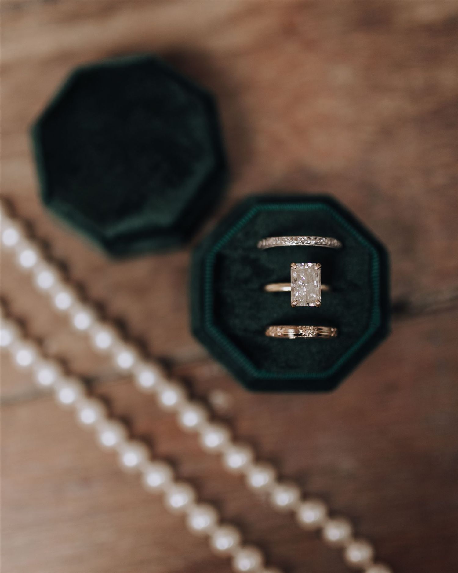 Diamond engagement ring and wedding band in dark green velvet ring box with pearl necklace.