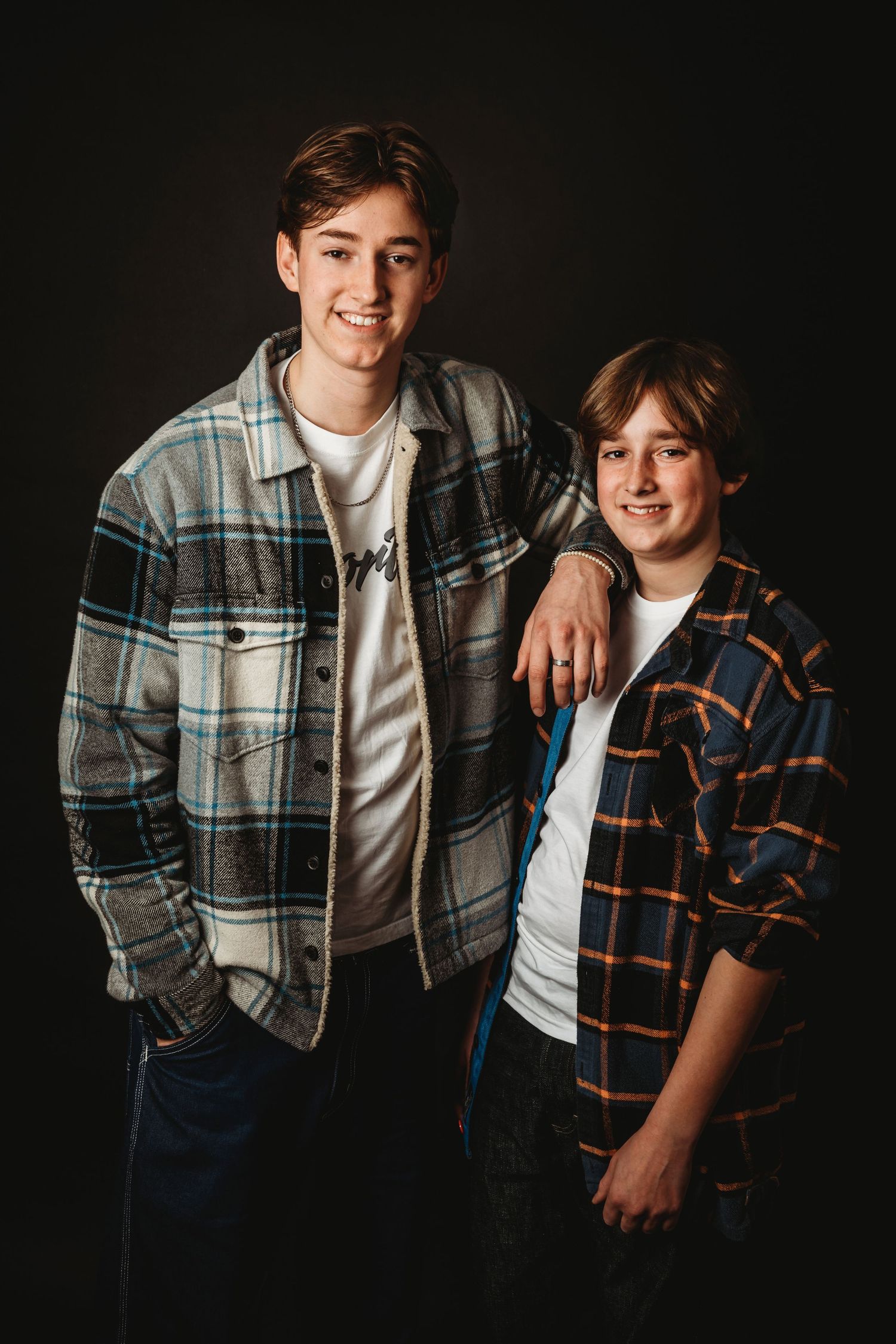 Two siblings wearing plaid flannel shirts and white t-shirts posing together against a dark background.