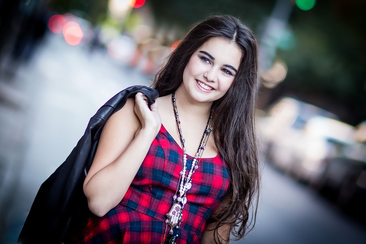 Smiling student in plaid top carries backpack while walking outdoors.