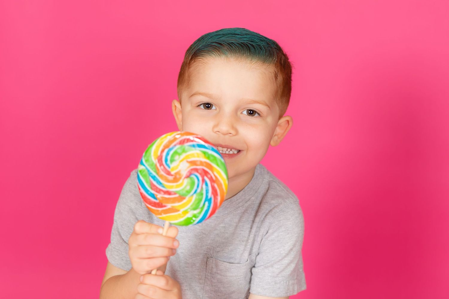 young boy with teal hair with bright lollipop on savage tulip pink backdrop in studio in clayton new jersey