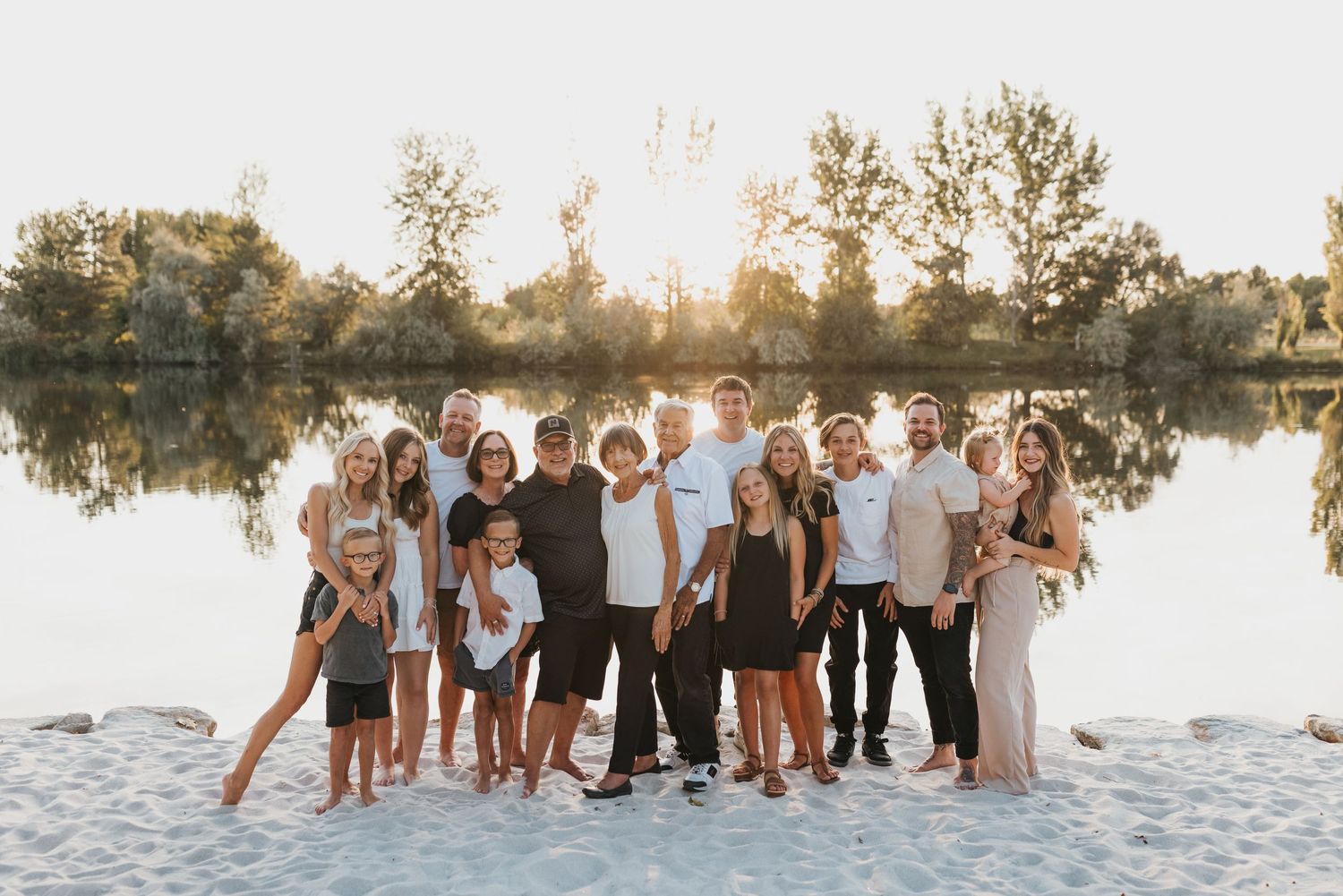 A large group poses together on a sandy beach at sunset with a lake reflection behind them.