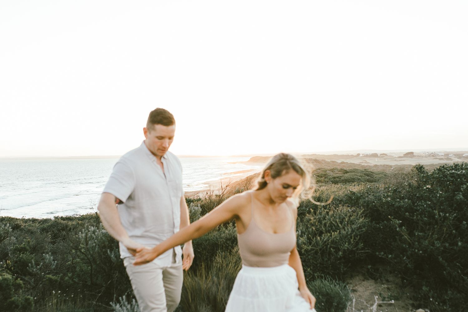 Playful couple walking along coastal cliffs during sunset with ocean views.