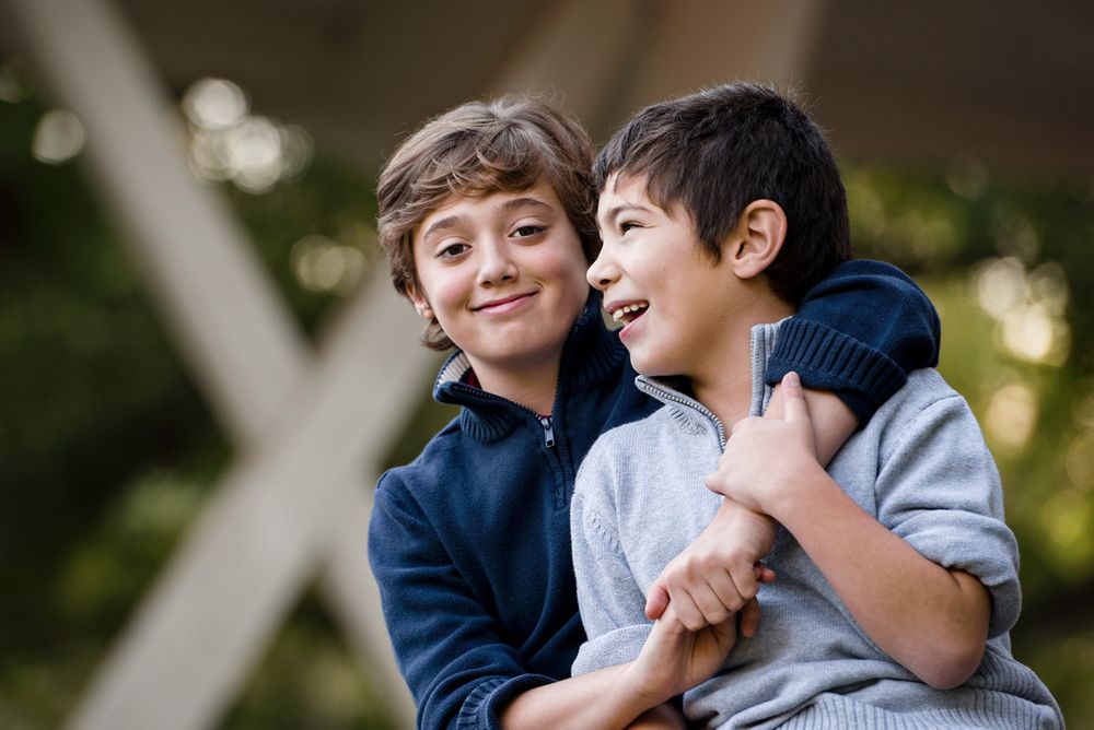 Two young boys in blue sweaters share a lighthearted laugh together outdoors.