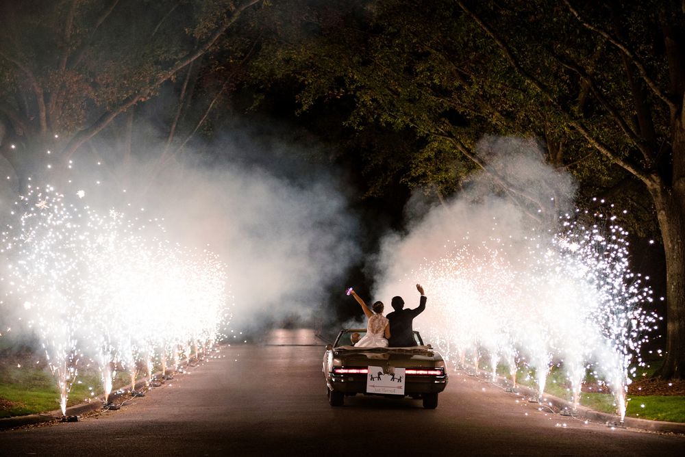 Wedding car exit with sparklers creating dramatic light show along tree-lined drive.