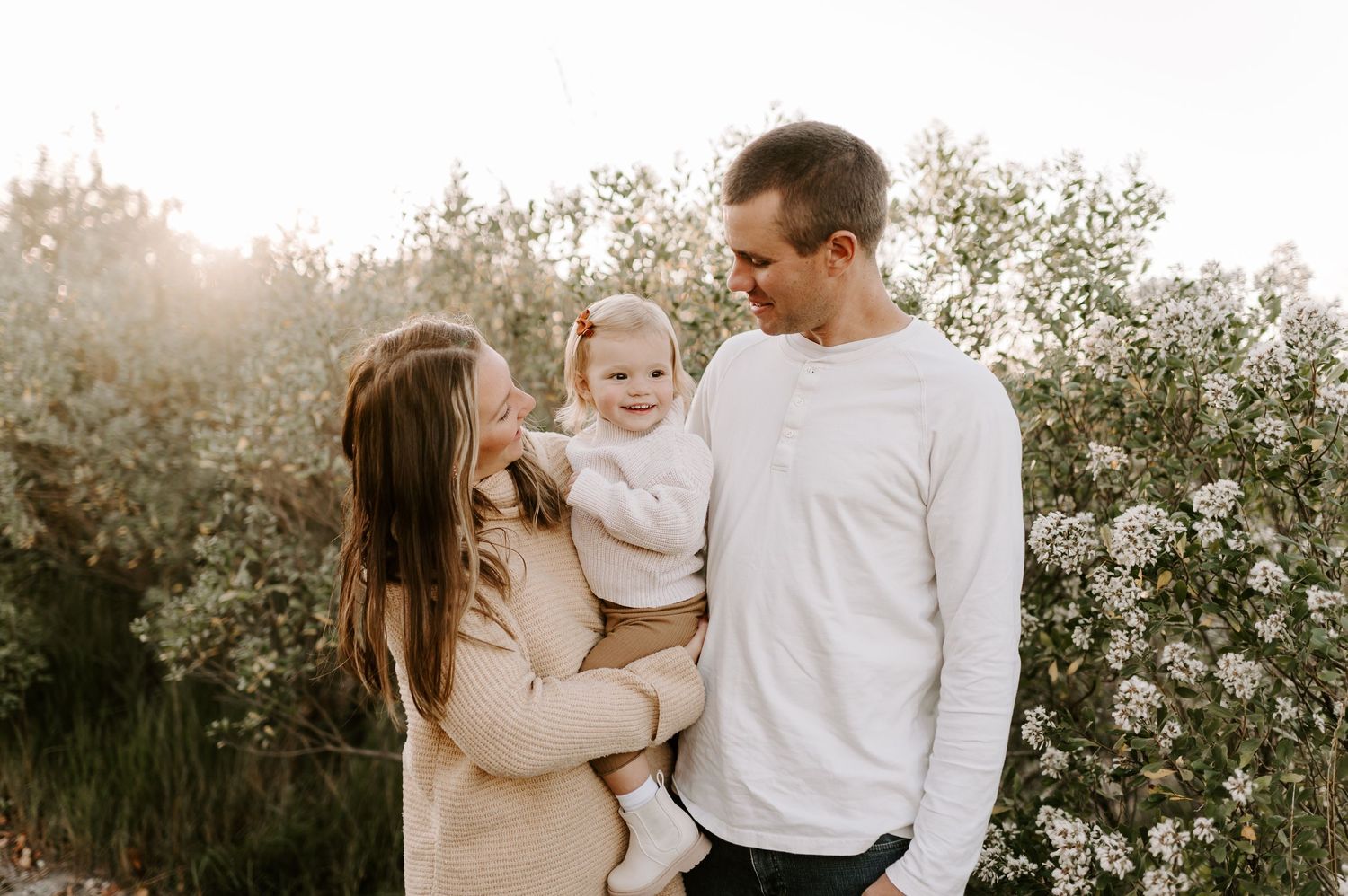 Family sharing tender moment among blooming white flowers at sunset.