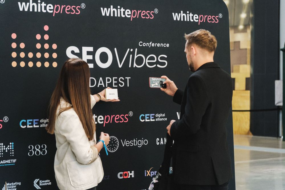 People interacting with SEO Vibes conference backdrop featuring white press branding.