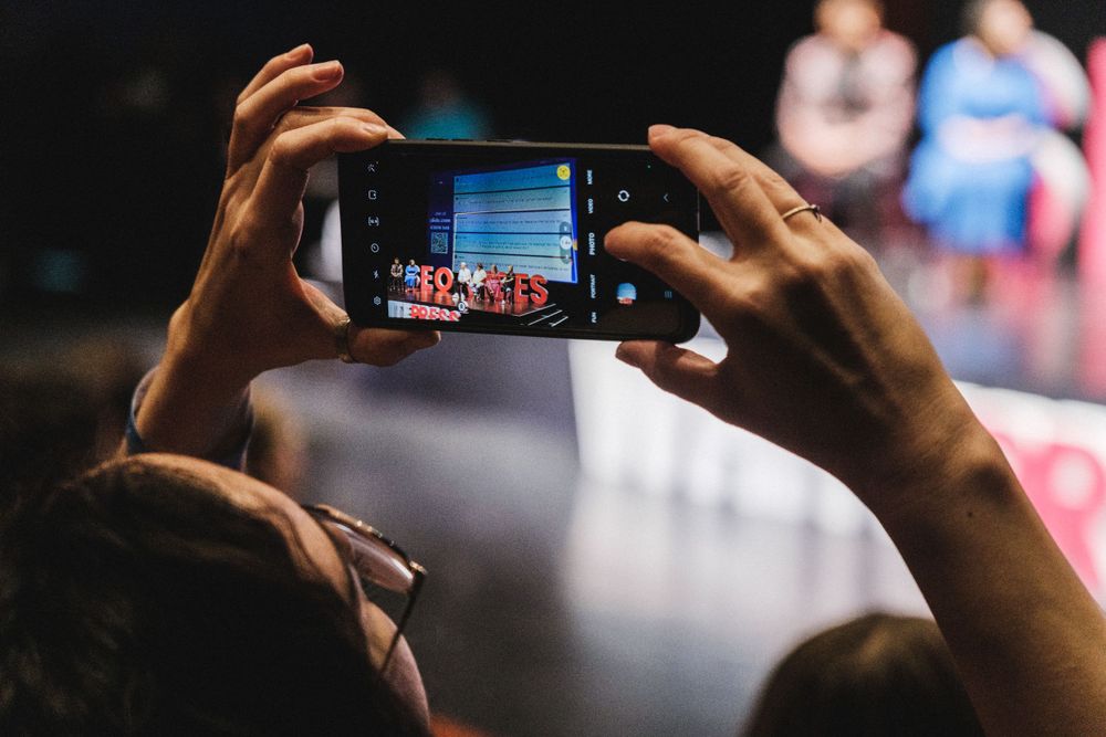 Hands holding smartphone to capture event stage performance.