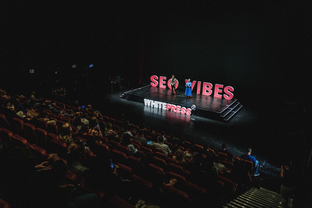 Illuminated SEO Vibes sign in a dark theater setting with audience seating visible.