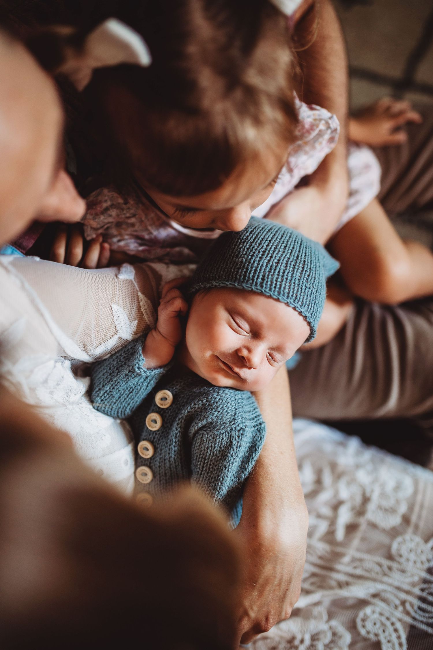 Sleeping newborn in blue knit outfit and hat held lovingly by family members.