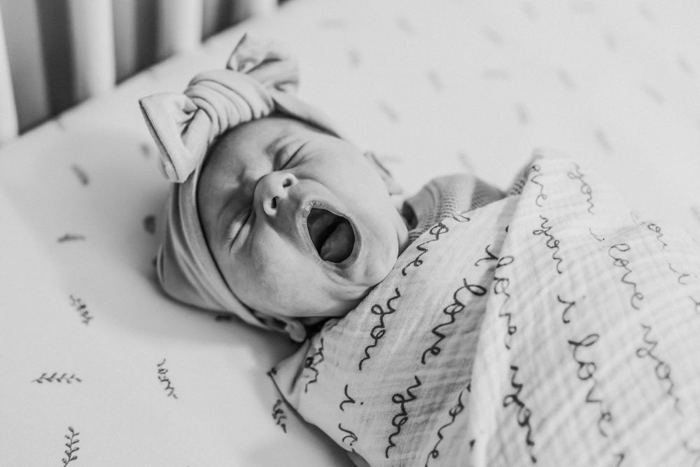 A little baby yawns in her crib during an in-home newborn session in Brunswick, Maine.