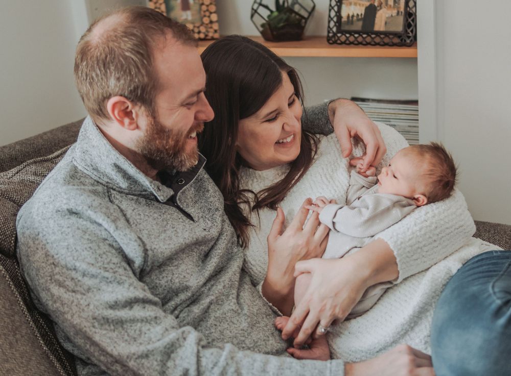 A mother and father look lovingly at their newborn daughter during an in-home newborn session in Brunswick, Maine.